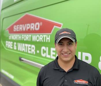 Male standing in front of tan wall next to sign reading Servpro One Team
